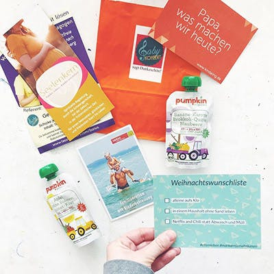 Die blaue Postkarte von Wishlephant, gehalten von einer Hand, daneben viele andere Produkte die im Goodiebag waren