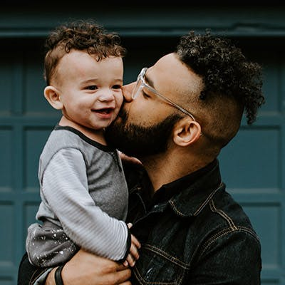Ein Vater trägt sein Kind im Arm und gibt einen Kuss auf die Wange.