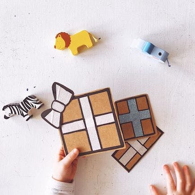 Eine Kinderhand hält kleine Geschenke, daneben sind Holztiere zu sehen.