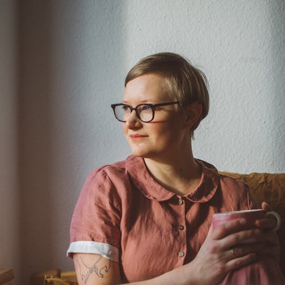 Marcia sitz auf einer Couch, mit einer Tasse in der Hand und schaut aus einem Fenster